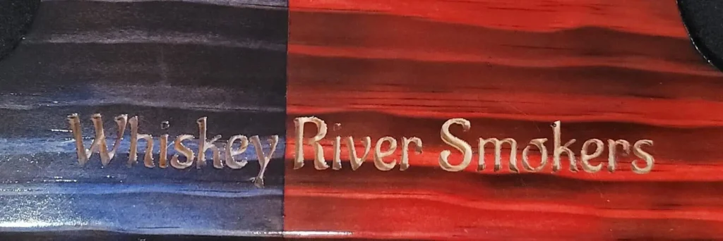 “Whiskey River Smokers” engraved on wood